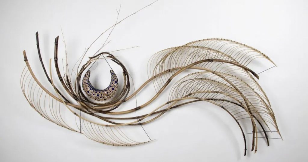 Journey of the Moon Charissa Brock Bamboo, glass, waxed linen thread, paper · 31 × 61 × 4 in A wide wall piece built from long curved bamboo canes, some dark and some pale, sweeping across from left to right. Thin bamboo ribs are stitched along several of the curves in fan-like rows.